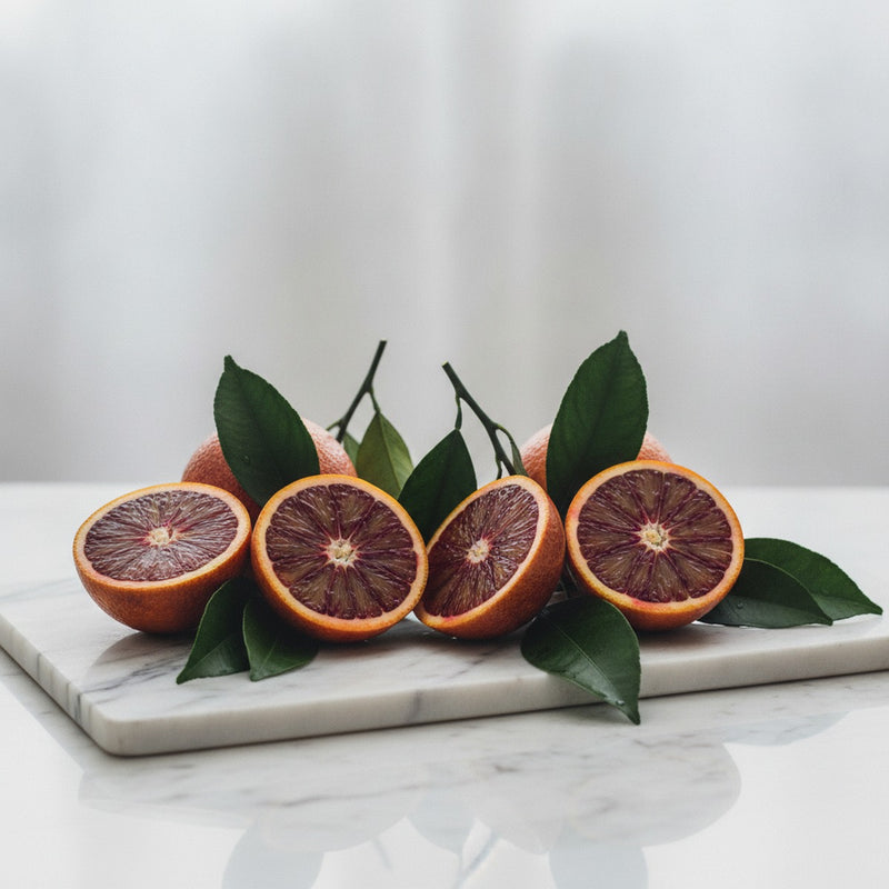 Blood Orange — Halved blood oranges with deep crimson flesh and glossy leaves arranged on white marble.