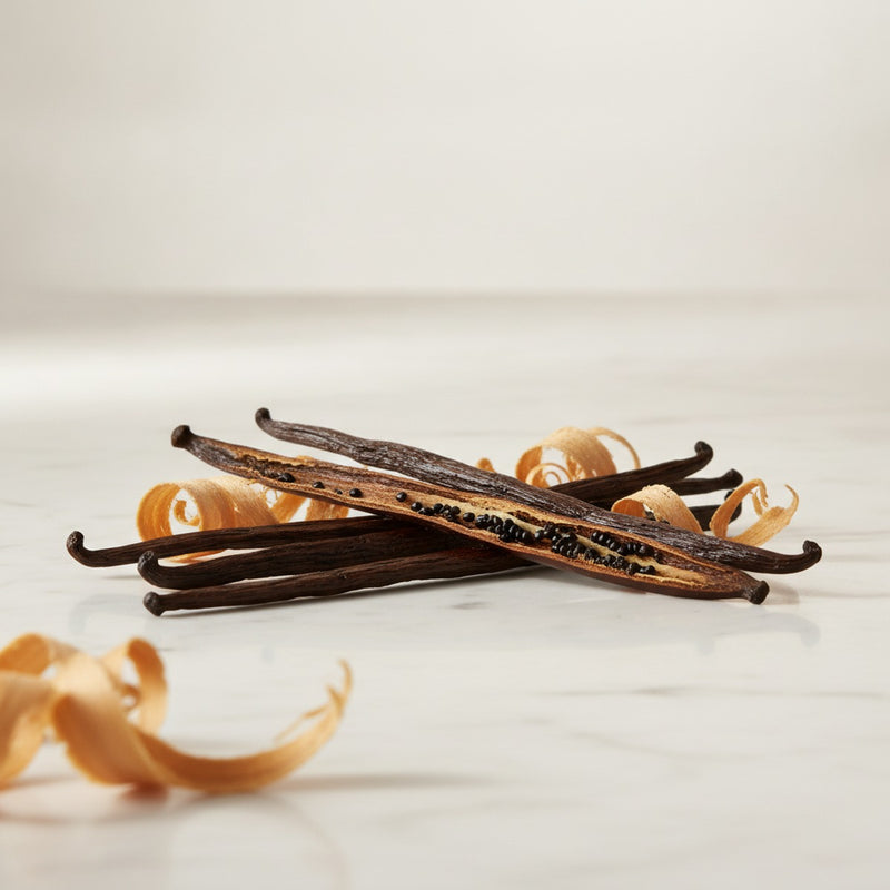 Bourbon Vanilla — Vanilla orchid pods split open with bourbon whiskey-soaked wood shavings on marble.