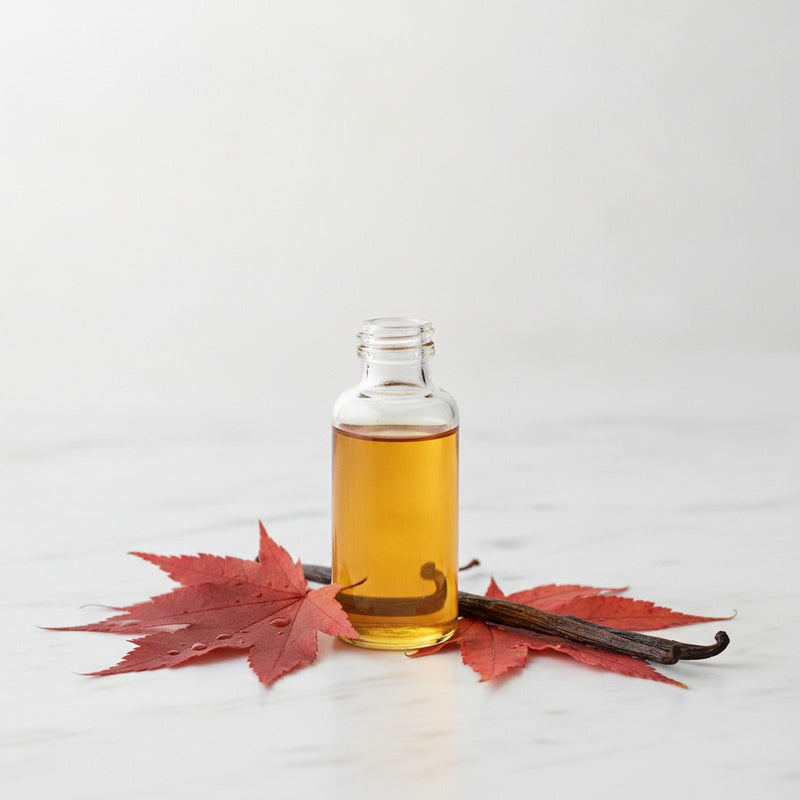 Maple Syrup — Amber glass vial of pure maple syrup beside fresh maple leaves and split vanilla bean on white marble.