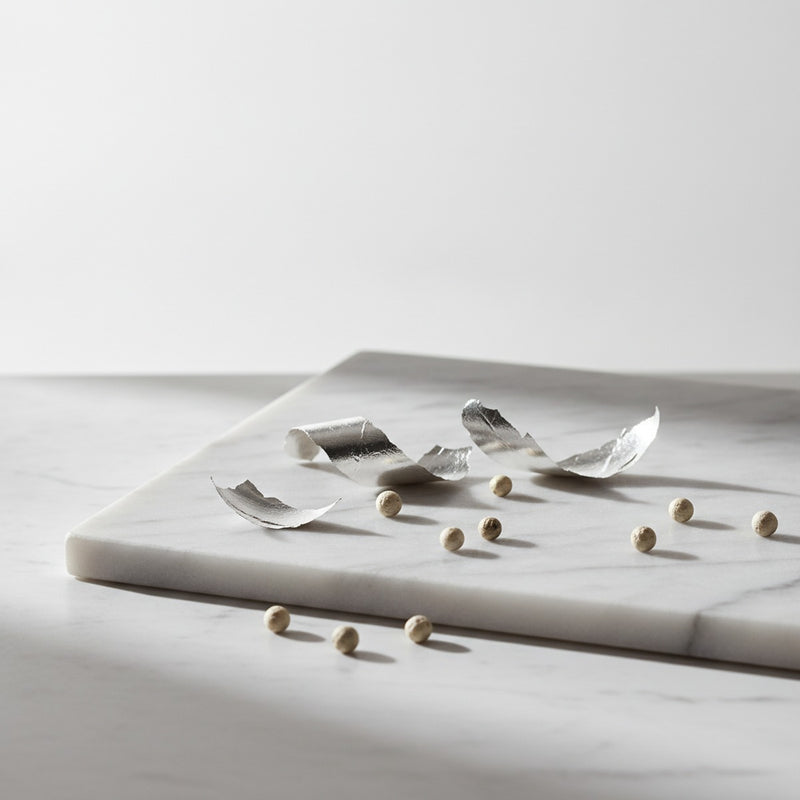 Metallic — Polished silver leaf and white pepper berries arranged on pale marble with soft morning light.