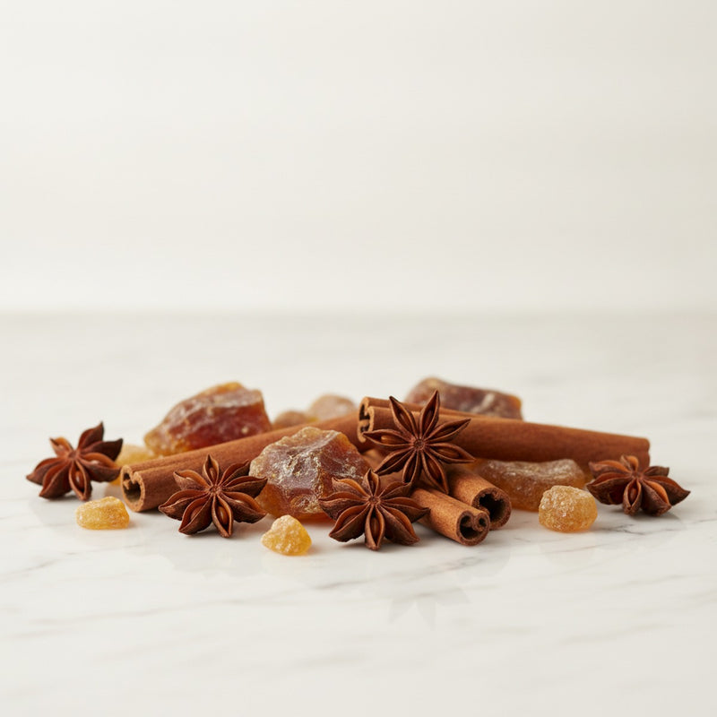 Spicy Amber — Scattered star anise, cinnamon sticks, and amber resin chunks on white marble.