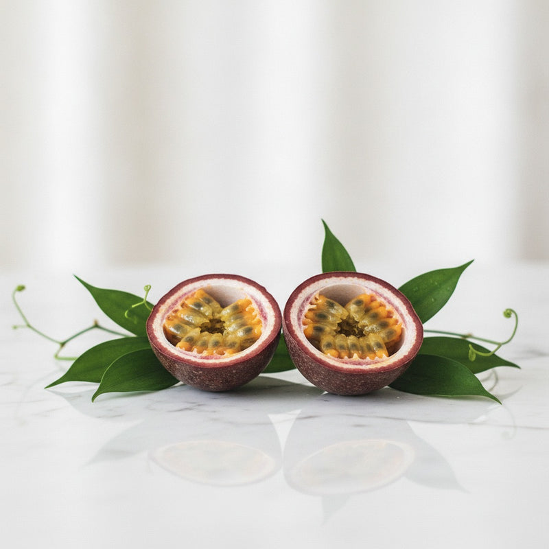 Passion Fruit — Halved passion fruits with seeds and pulp glistening on white marble, surrounded by fresh green leaves.
