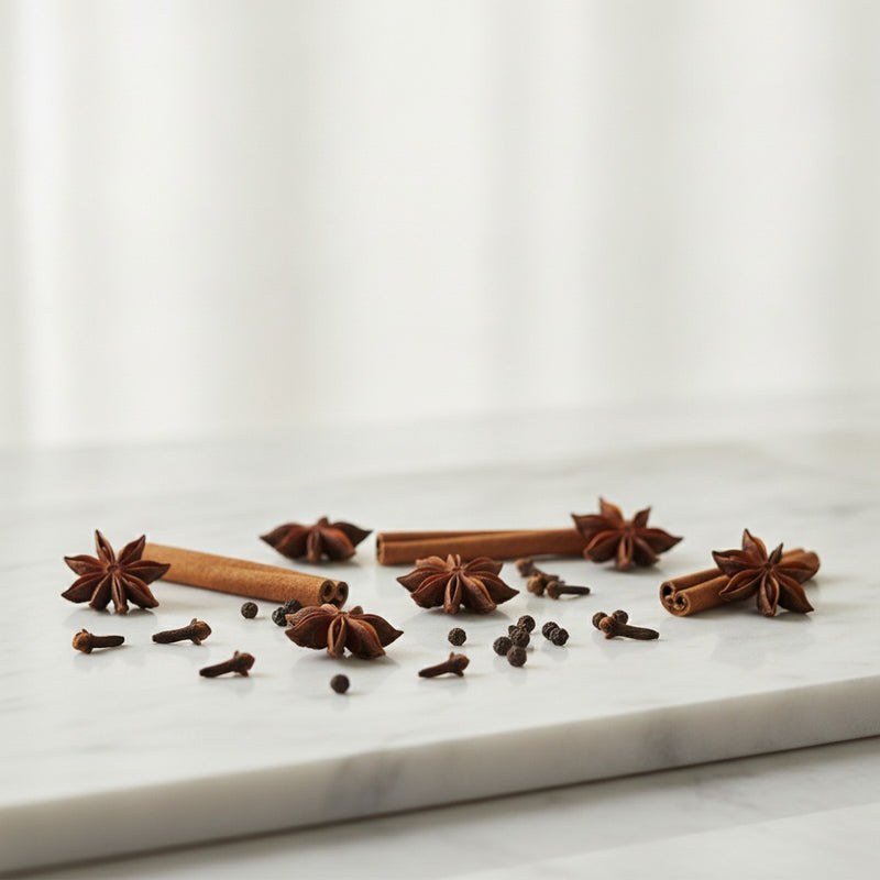 Spicy — Scattered whole spices—star anise, cinnamon sticks, black peppercorns, cloves—on pale marble.